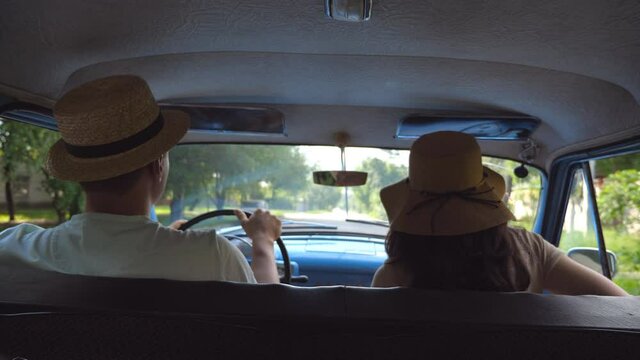 Young couple in hats driving on country road in classic vintage car. Unrecognizable pair riding into old auto. Man and woman sitting at the front seat of a retro automobile. Trip concept. Slow motion