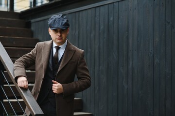 A man walks at city street in the image of an English retro gangster of the 1920s dressed in Peaky blinders style.