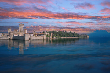 Sirmione, Lake Garda, Italy. The famous Sirmione Castle, good weather. Castle reflections in the water. Pink clouds at sunrise.