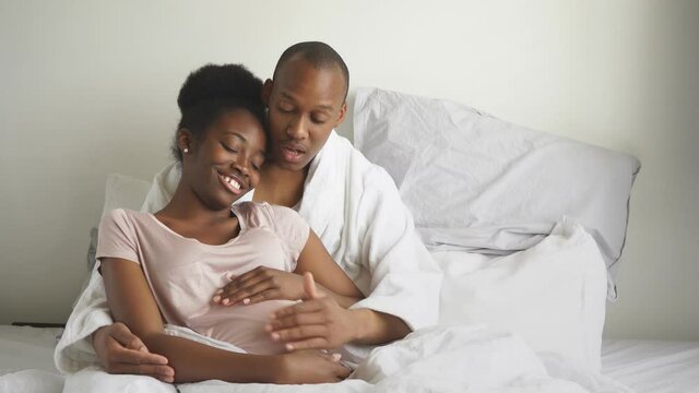 Happy family will have replenishment soon, pregnant woman and man lie on bed in morning, at home.
