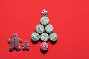 Gingerbread family standing by a Christmas tree made of macarons with a gingerbread star topper on a red background