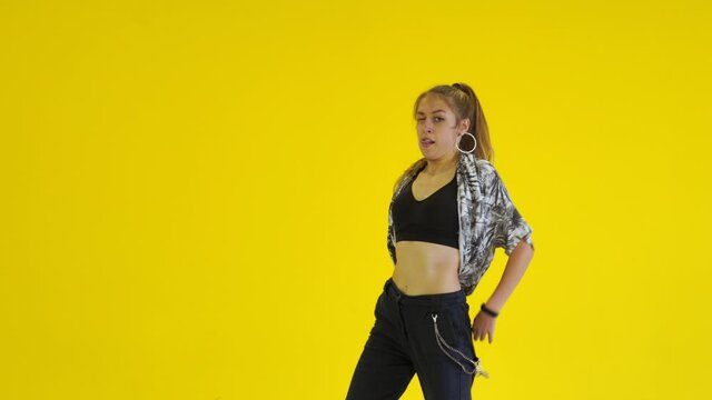 Young energetic woman dancing modern youth dance free style in the studio against the background of a yellow wall. Isolated. Medium long shot