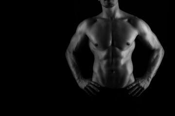 Fototapeta premium Muscular male torso of fit bodybuilder on black background in black and white