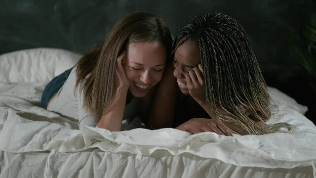 Homosexual family of mixed ethnicity. Lesbian couple lie in bed chatting, laughing and hugging