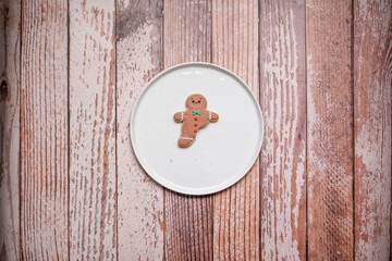 Christmas gingerbread man cookie partially eaten with icing and decorations on a white plate on a weathered wooden table background with copy space and room for text.