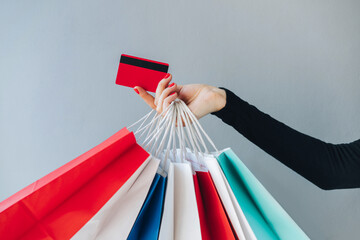 Close up crooped shot of woman hand holding many paper handbags and red credit card