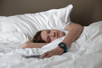 White teenager lies sad alone in bed with a smartphone. Loneliness. Insulation. Quarantine