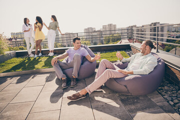 Photo of two young happy joyful smiling cheerful men sit armchair drink champagne talk communicate...