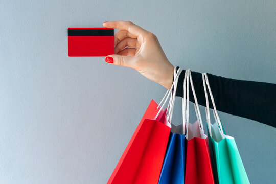 Close up crooped shot of woman hand holding many paper handbags and red credit card