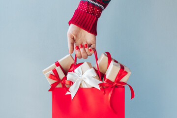 Cropped image of female hand with red polished nails holding shopping bag full of christmas gift boxes - 391490201