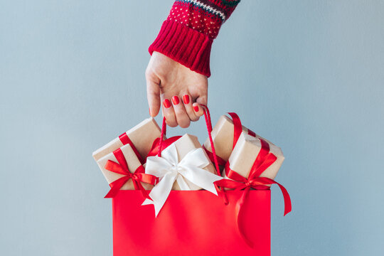 Cropped image of female hand with red polished nails holding shopping bag full of christmas gift boxes