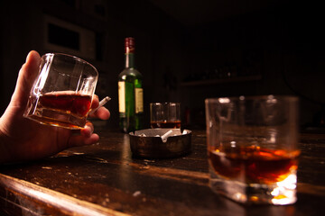 Hands holding a cigarette smoking and drinking alcohol. Glass of whiskey, cigarettes and ashtray