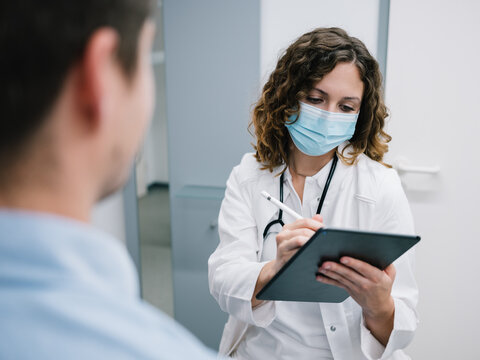 Junge &Auml;rztin geht den Anamnesebogen mit einem neuen Patienten durch
