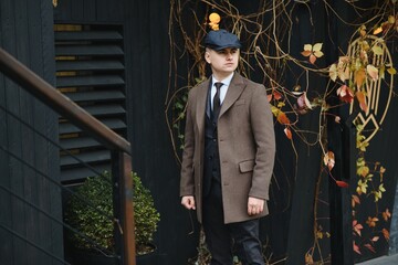 A man posing in the image of an English retro gangster of the 1920s dressed in a coat, suit and...