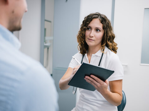 Junge &Auml;rztin geht den Anamnesebogen mit einem neuen Patienten durch