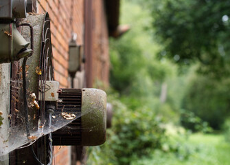 Rusty cooling ventilator on back of an old derelict barn. The electric fan is covered by a spider web. farm in middle Germany.