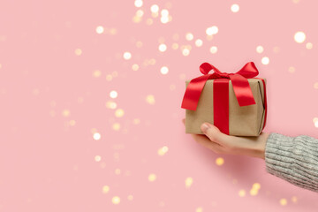 Hand hold gift box tied with red ribbon on a pink background. Festive shiny concept.