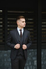 Fototapeta premium Portrait of handsome fashion businessman model dressed in elegant suit. Man posing on street background. Metrosexual