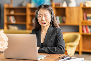 Happy asian businesswoman in headset speaking by conference call and video chat on laptop in...