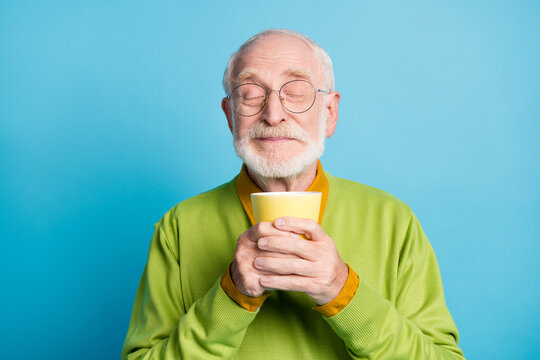 Photo Of Pensioner Old Man Hold Cup Eyes Closed Sniff Aroma Wear Eyeglasses Green Pullover Isolated Blue Color Background