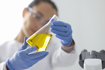 Gloved scientist holds flask with golden liquid. Oil and its useful properties concept