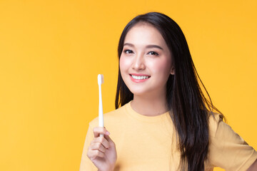 Beauty portrait young asian woman holding toothbrush and smiling on yellow background. Concept good oral and dental health.