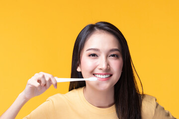 Beauty portrait young asian woman holding toothbrush and smiling on yellow background. Concept good oral and dental health.