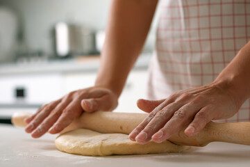 Close-up of a woman rolls out the dough with a rolling pin.