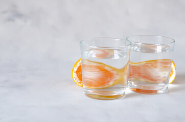 Mandarin citrus fruits reflecting through a glass cup with water on a gray background. Distorted water image. Art concept. Minimalism. Copy space. Abstraction. Perspective, fractured and skewed images