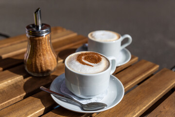Cappuccino with whipped foam and chocolate chip pattern. Cups with hot aromatic coffee drinks standing on a wooden table, in a coffee shop, on the street.
