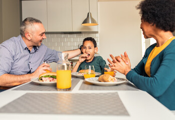 Fototapeta na wymiar Smiling mixed race family sitting at the kitchen table having breakfast at home. 