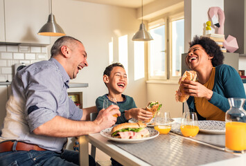 Smiling mixed race family sitting at the kitchen table having breakfast at home.	