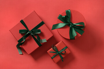 Christmas three gifts wrapped in red paper and decorative green rope ribbon on red surface....