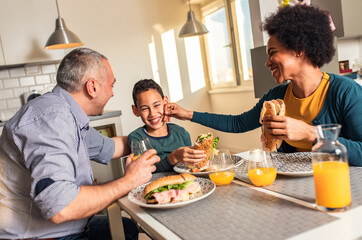 Smiling mixed race family sitting at the kitchen table having breakfast at home.	