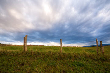 Angular view of fence and blue sky with white clouds, green meadows in a town in Cantabria, Spain, horizontal