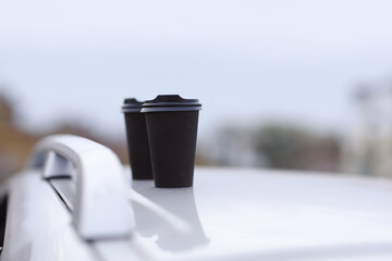 Two black glasses of drinks in a stand on a blurred background of the city. Take-out coffee or tea in disposable cups. A quick snack. Coffee cups on the car. selective focus