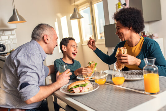 Smiling mixed race family sitting at the kitchen table having breakfast at home.	