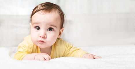 Fototapeta premium Cute funny little child lying on bed on white background with copy space. little baby girl learning to crawl and playing in bedroom.