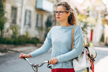 Pretty student female going to the university with a bike on a sunny day outdoors. Pretty woman in...
