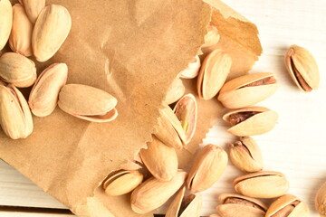 Organic salted delicious pistachios with a paper bag, close-up, on a white wooden table.
