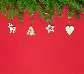 Fototapeta na wymiar Christmas border with fir branches and wooden Christmas tree toys on red with copy space. new year card
