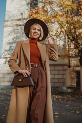 Outdoor autumn fashion portrait of elegant happy smiling woman wearing trendy midi beige, camel...