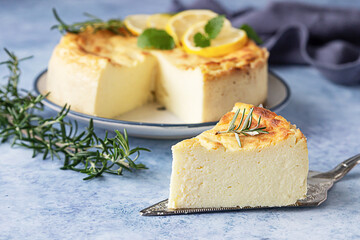 Lemon vanilla cheesecake decorated with rosemary, mint and lemon slices. Ricotta no crust cheesecake or casserole. Blue concrete background.