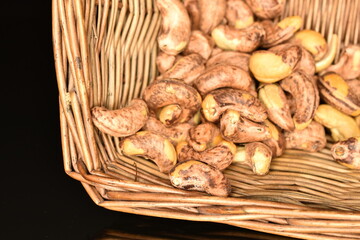 Fragrant roasted cashews in a basket of vine, close-up, on a black background.