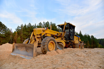 Motor Grader on road construction in forest area. Greyder leveling the sand, ground and gravel...