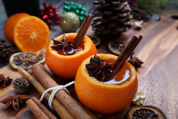 christmas hot mulled wine infused with star anise and cinnamon in the orange peel are on the wooden table during christmas new year celebration party with happy family in the warm cottage background