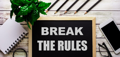 BREAK THE RULES is written in white on a black board next to a phone, notepad, glasses, pencils and...