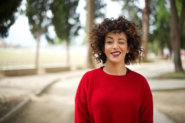 Coquettish Young arab woman wearing casual red sweater in the street smiling happily, blinking at...