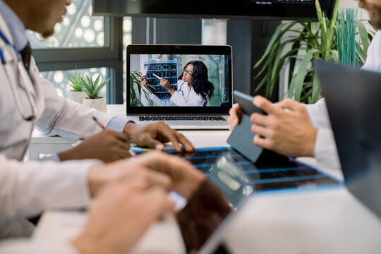 Cropped image of multiracial doctors using laptop for video conference with African female colleague, discussing CT scan results and making notes on tablets. Focus on African woman on laptop screen