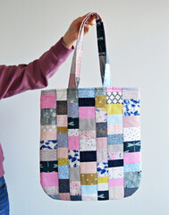 Hand holding colorful quilted patchwork tote bag over white